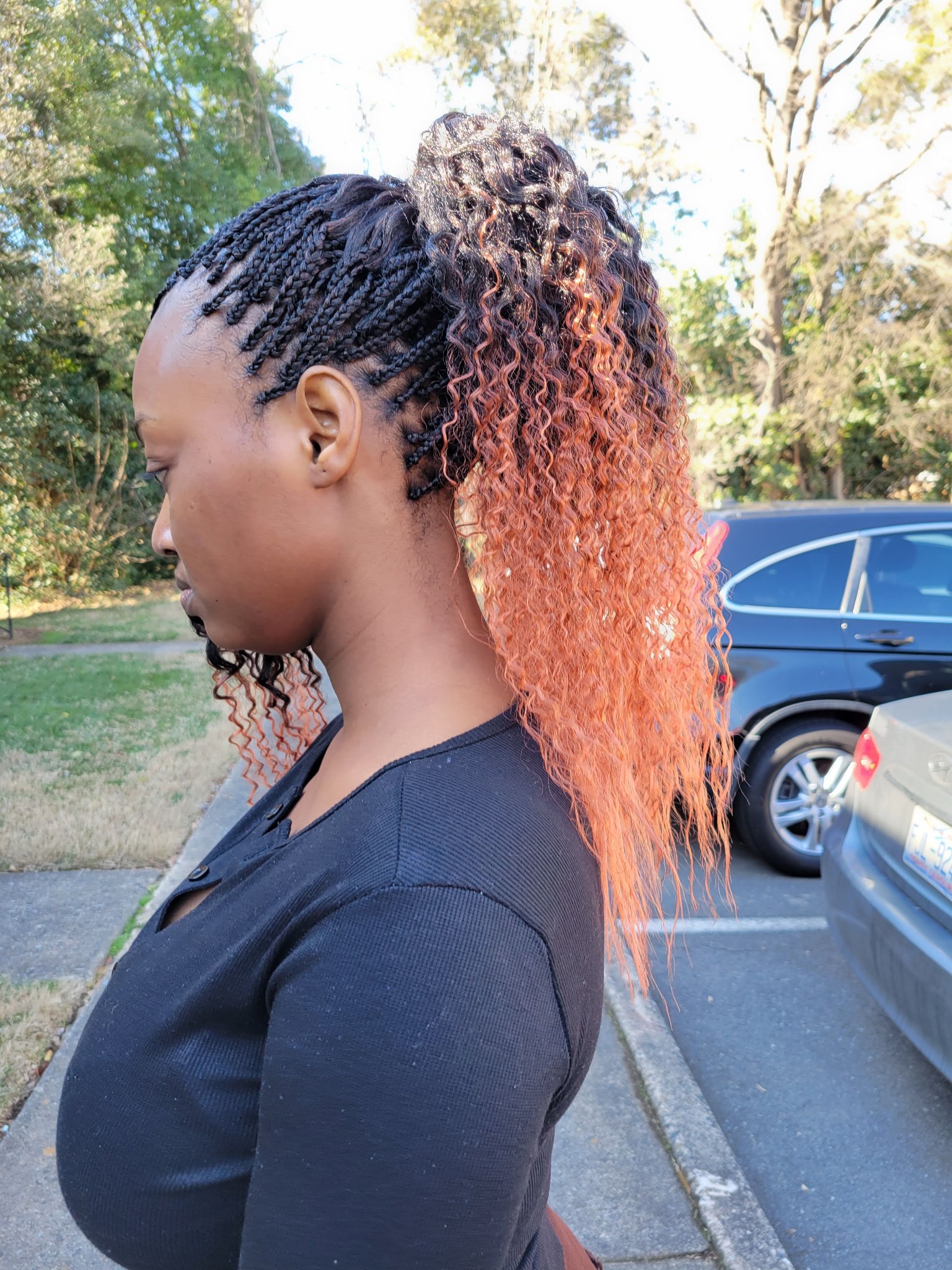 Micro braids in black gathered into a high ponytail with copper ombre curly ends, side view